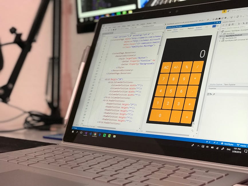 A close-up view of a silver laptop displaying a code editor with syntax-highlighted HTML and CSS on the left side, and a digital calculator interface with orange buttons on the right, situated on a de