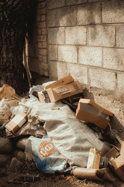 In this outdoor urban scene, a collection of overflowing rubbish bins and scattered waste materials occupy a paved sidewalk area near a small parking space. The central focus is on a large, gray mixed